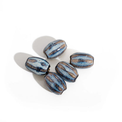 Five handmade ceramic beads with a glossy finish, featuring a blue and brown striped pattern with dark metallic accents, arranged on a white background with soft shadows.