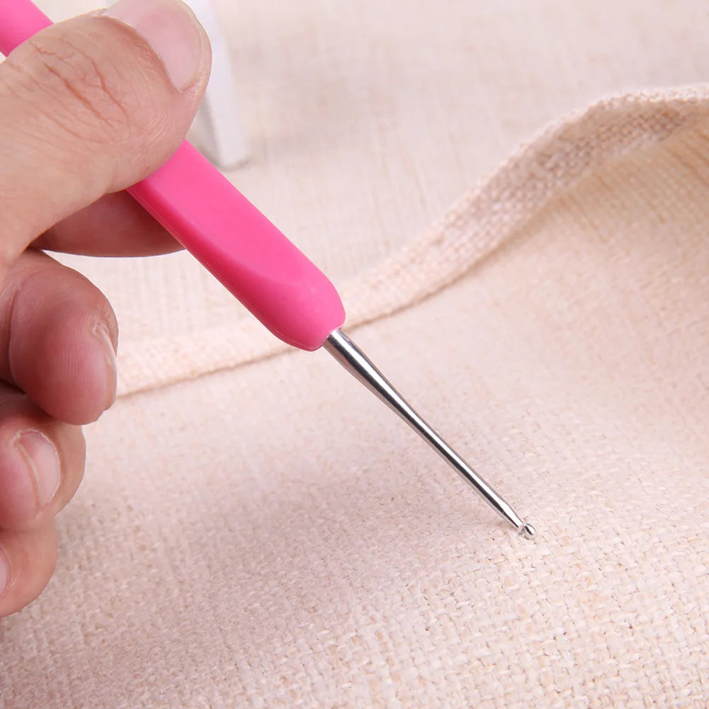 Hand holding a pink crochet needle against a beige fabric background