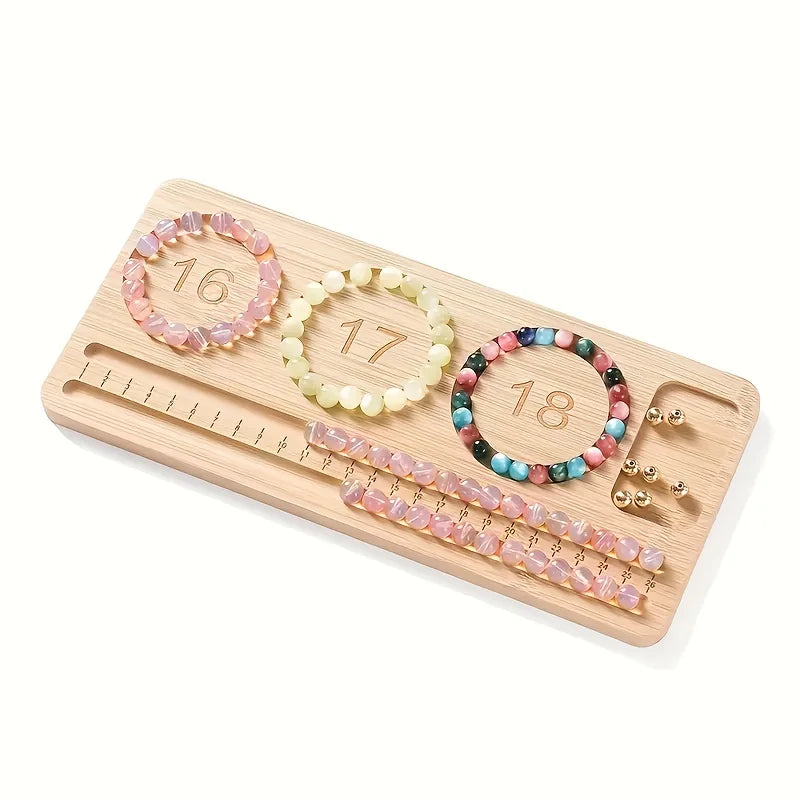 A wooden bead board organizer tray displaying three beaded bracelets, a row of pink beaded chains, a pair of gold stud earrings, and a ruler scale on a white background.
