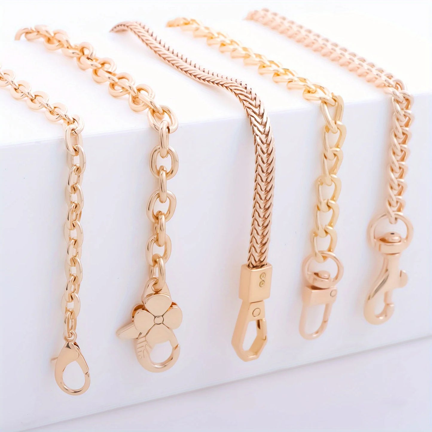 Four rose gold chain accessories with different link styles and clasp designs, arranged on a white display block.