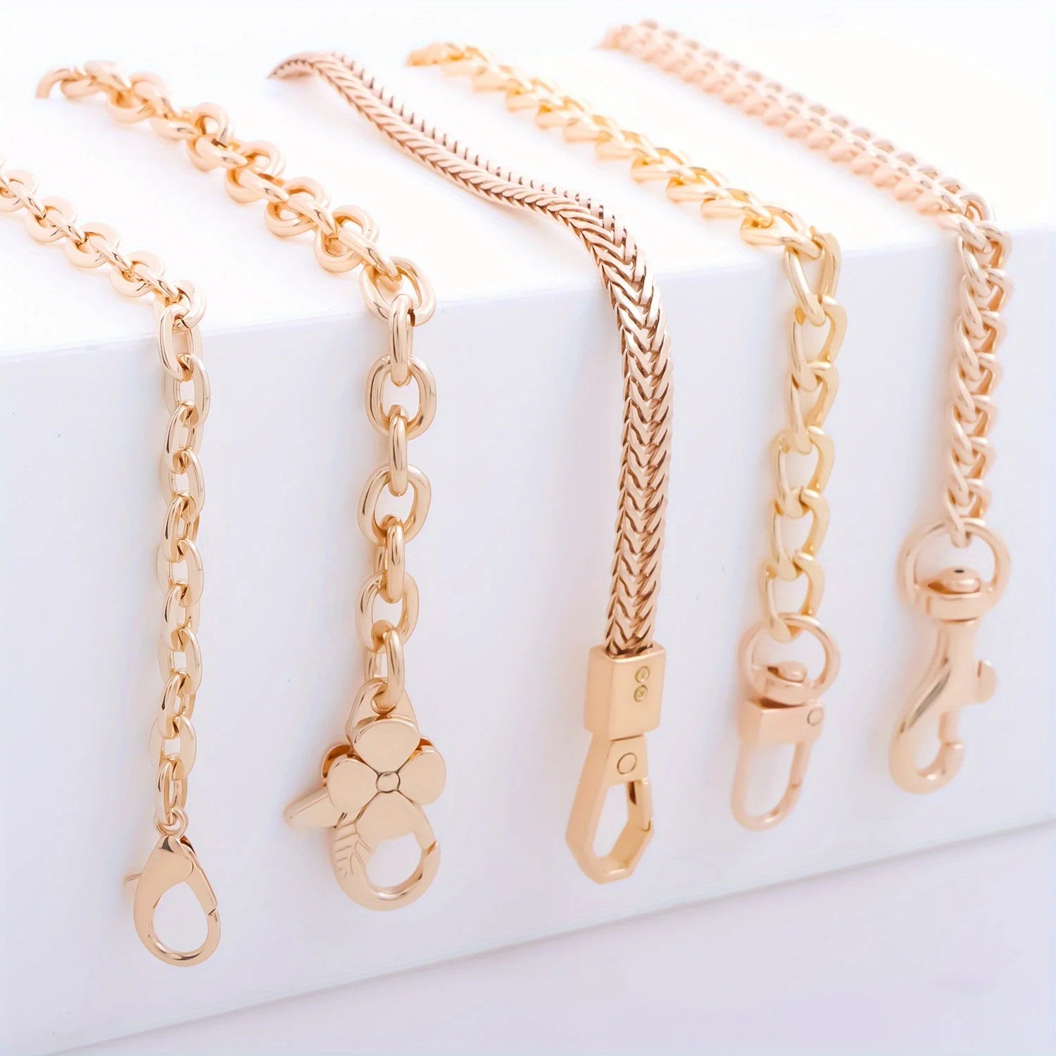 Four rose gold chain accessories with different link styles and clasp designs, arranged on a white display block.