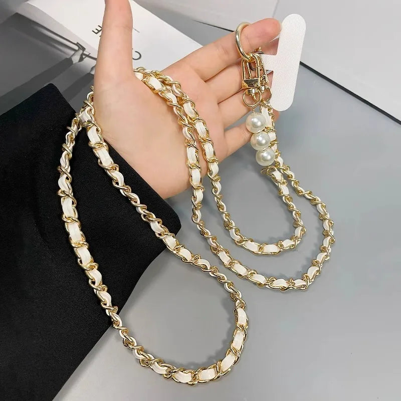 Gold and pearl chain strap held by a hand on a gray surface