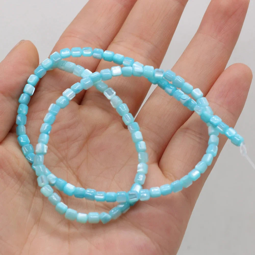 A strand of small light blue faceted shell beads draped across an open hand, showing the color and shape of the beads against the skin.