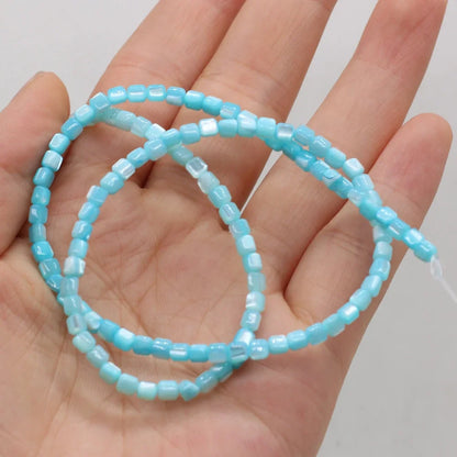 A strand of small light blue faceted shell beads draped across an open hand, showing the color and shape of the beads against the skin.