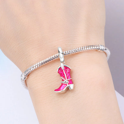A silver-toned twisted bangle bracelet with a dangling cowboy boot charm in bright pink enamel, shown worn on a person's wrist.