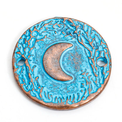 A round turquoise and copper pendant featuring a raised crescent moon in the center, with two pre-drilled holes on the sides, shown on a plain white background.