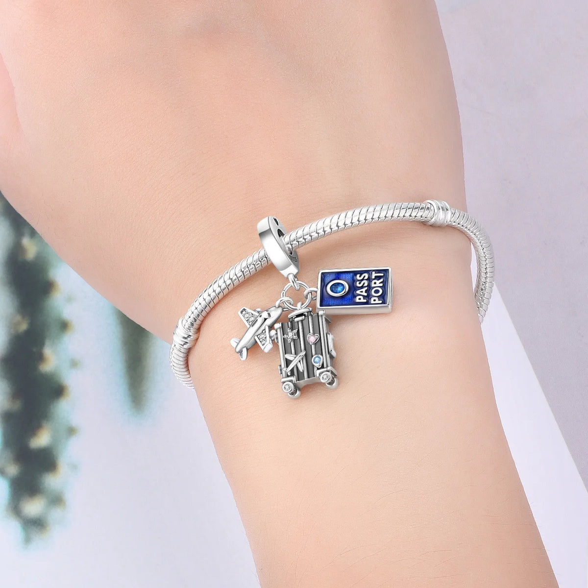 Silver bracelet with travel-themed charms on a wrist against a neutral background