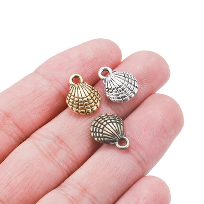 Three small seashell-shaped jewelry charms in gold, silver, and antique bronze finishes, displayed on a person's fingers against a white background.