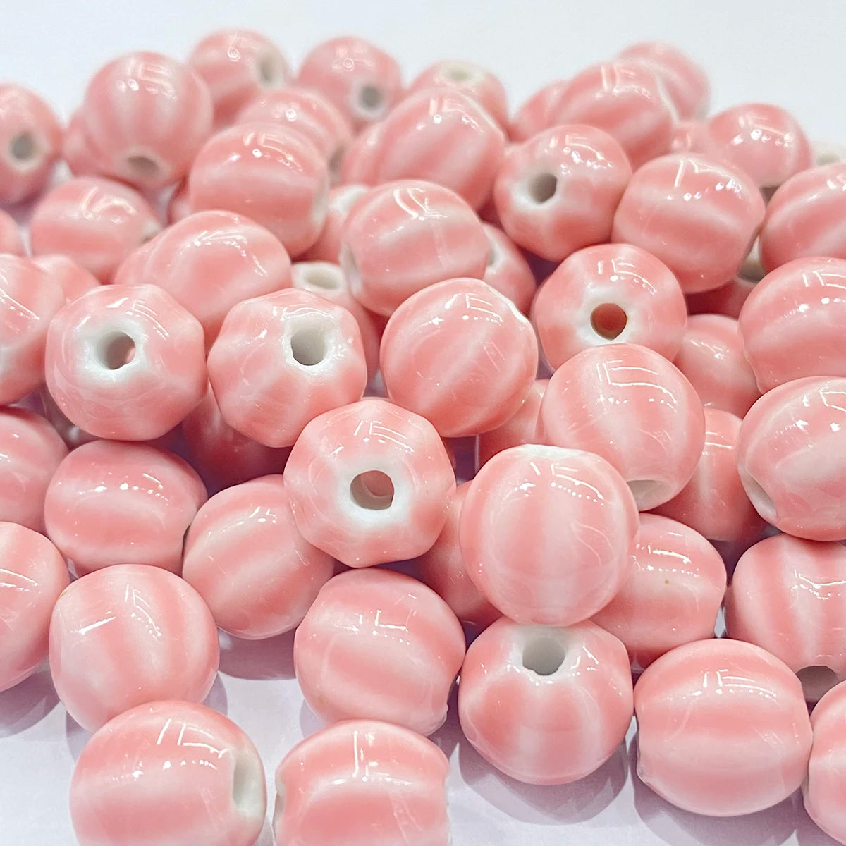 A pile of glossy pink and white striped ceramic beads with a central hole, arranged closely together on a white background.