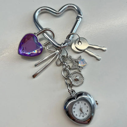 Heart-shaped keychain with charms including a clock, purple heart, and key on a light gray background