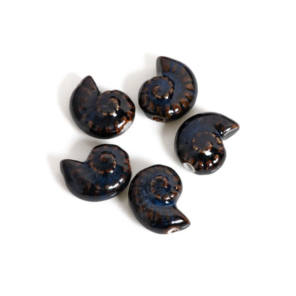 Five glossy spiral-shaped beads resembling ammonite shells, featuring a dark blue and black base with brown mottled details, arranged on a plain white background.