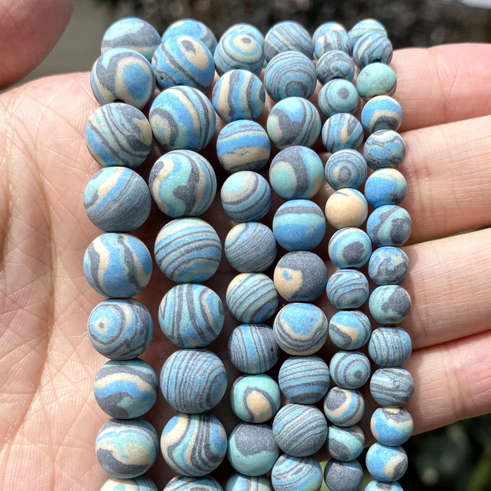 Multiple strands of round marbled beads in shades of blue, gray, and cream, held in a person's hand.