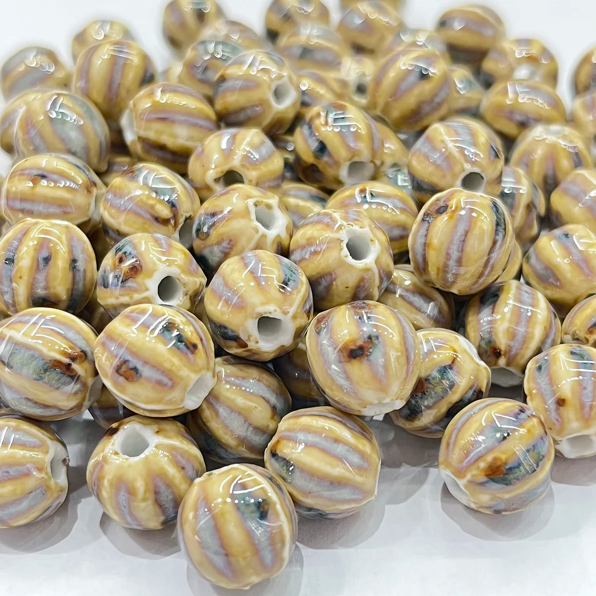 A pile of round, glossy ceramic beads with a striped pattern in beige, brown, and gray, each featuring a hole drilled through the center.