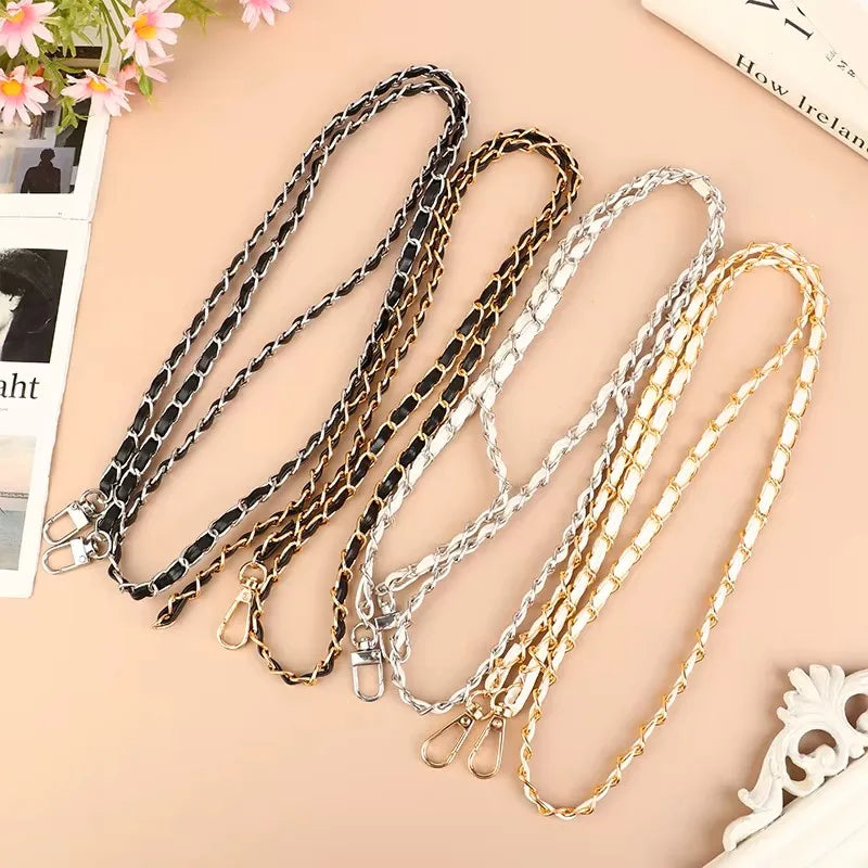 Four bag chain straps in black, gold, and silver on a beige surface.