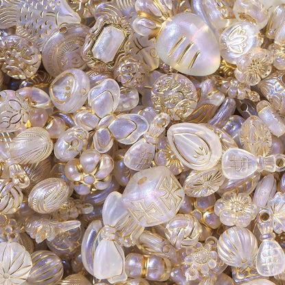 A dense pile of decorative glass beads in iridescent milky white and pale gold, featuring various shapes including pearls, floral motifs, ribbed textures, and gold foil accents.