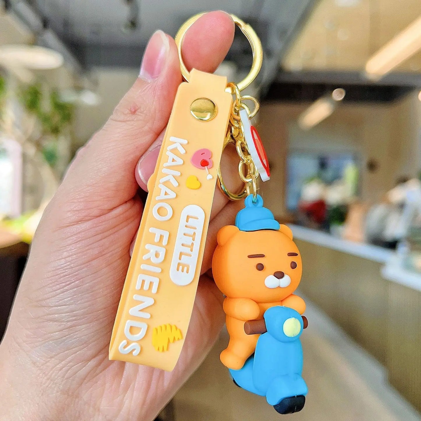 Hand holding a keychain with a character from 'Kakao Friends' in an indoor setting.