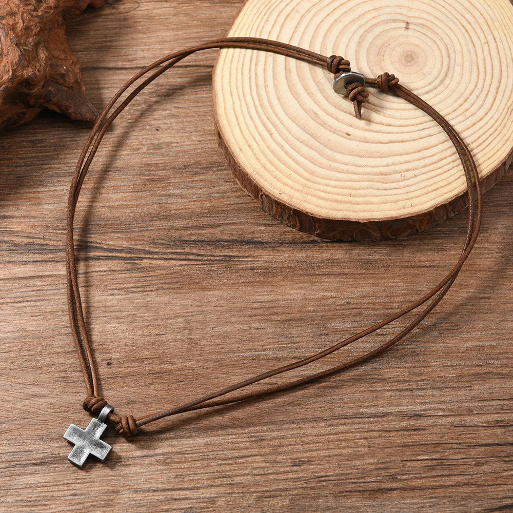 Brown leather cord necklace with a silver cross pendant on a wooden surface