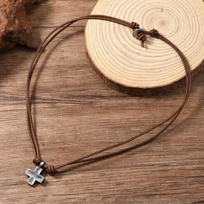 Brown leather cord necklace with a silver cross pendant on a wooden surface