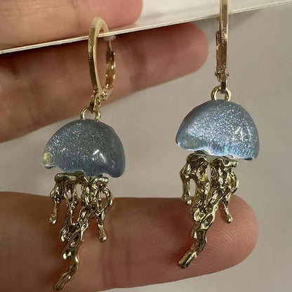 Jellyfish-shaped earrings with gold details held between fingers against a neutral background