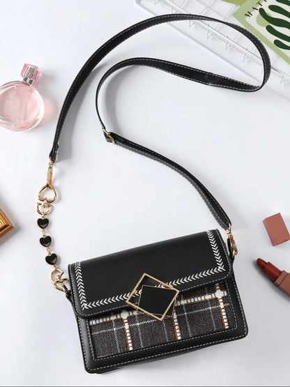Black handbag with plaid pattern and decorative strap on a white surface
