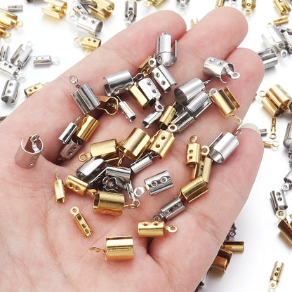 A hand holding a pile of small bead cap jewelry findings in gold and silver finishes, with more of the same scattered around on a white background.