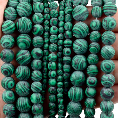 Multiple strands of round green malachite beads with natural swirling patterns, held in a hand against a white background.