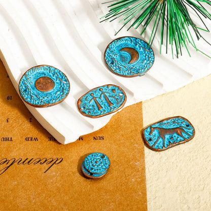 Five turquoise-blue carved wooden beads with rustic brown edges, featuring various symbols and designs, arranged on a styled flat-lay background of white slatted paper, kraft paper, and a green pine branch.