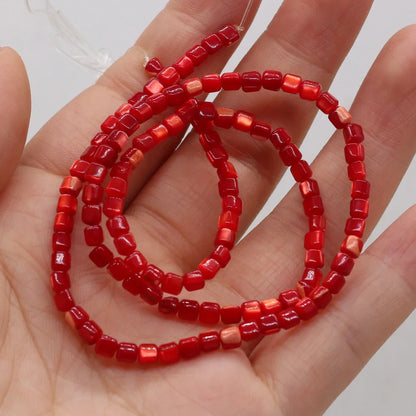 A hand holding a strand of small red faceted shell beads, with some translucent pale pinkish-red beads mixed in, against a plain light background.