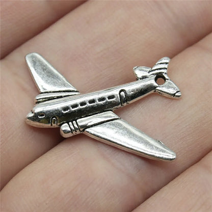 Silver airplane pendant on a person's finger. Travel charms for jewelry making featuring airplane, passport, suitcase and camera charms.