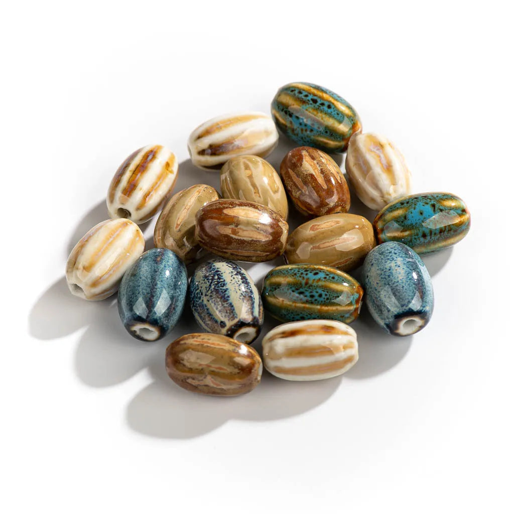 A pile of glazed ceramic seed beads with various patterns including blue and green speckles, brown and cream stripes, and solid brown and cream colors, arranged on a white background.