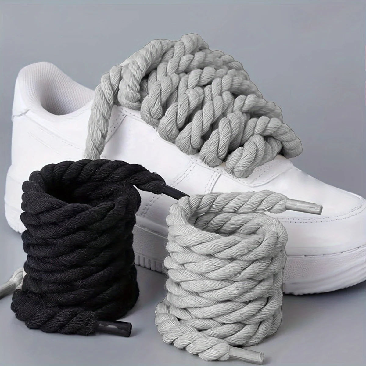 White sneakers with black and gray ropes on a light gray background