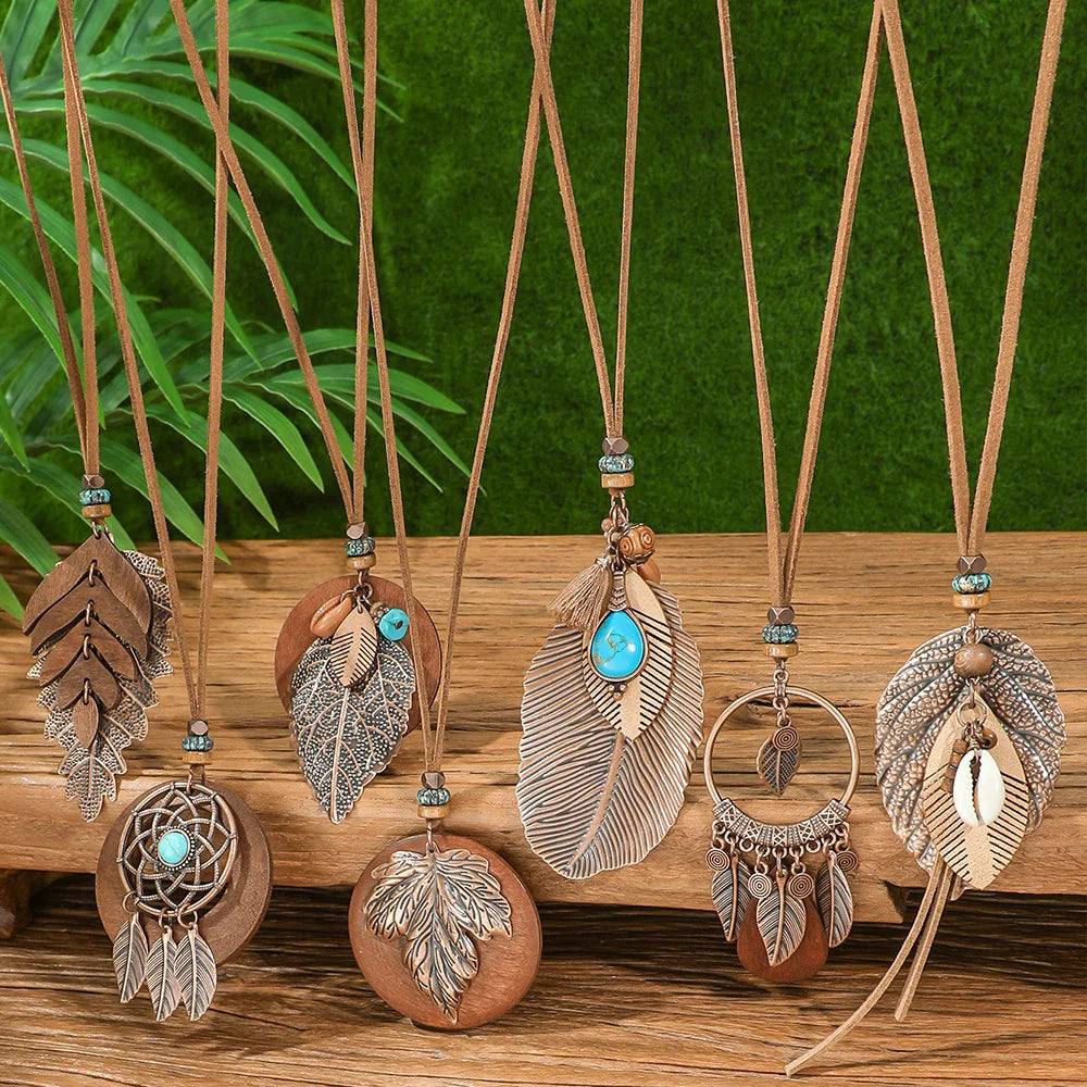 Necklaces with feather and leaf pendants on a wooden surface with a green leafy background