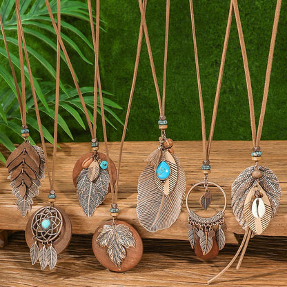 Necklaces with feather and leaf pendants on a wooden surface with a green leafy background