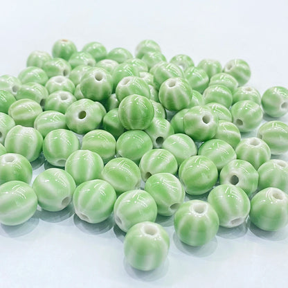 A pile of glossy, light green ceramic beads with a ribbed, pumpkin-like texture and a central hole, arranged on a clean white background.