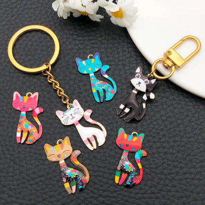 Colorful cat-shaped keychains on a dark textured surface with white flowers.