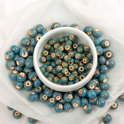 Blue speckled seed beads with brown and cream rings, arranged around a small white bowl on a white fabric background.