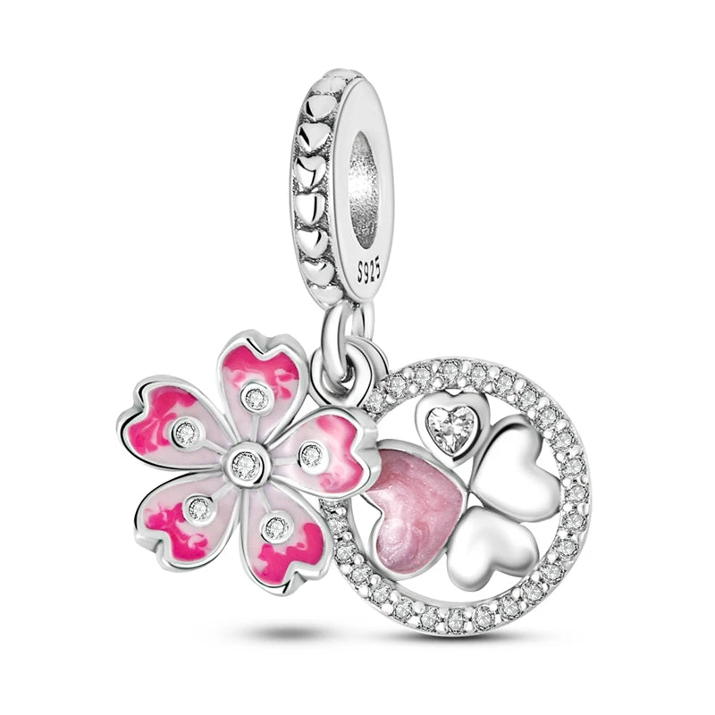 A sterling silver charm dangle featuring a pink and silver cherry blossom flower, a silver four-leaf clover with a pink heart-shaped center, and a silver heart, all adorned with clear rhinestones and set against a white background.
