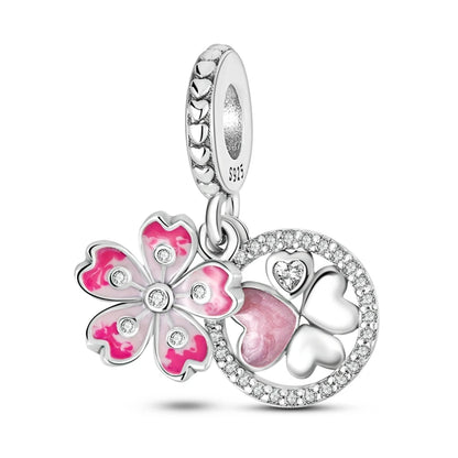 A sterling silver charm dangle featuring a pink and silver cherry blossom flower, a silver four-leaf clover with a pink heart-shaped center, and a silver heart, all adorned with clear rhinestones and set against a white background.