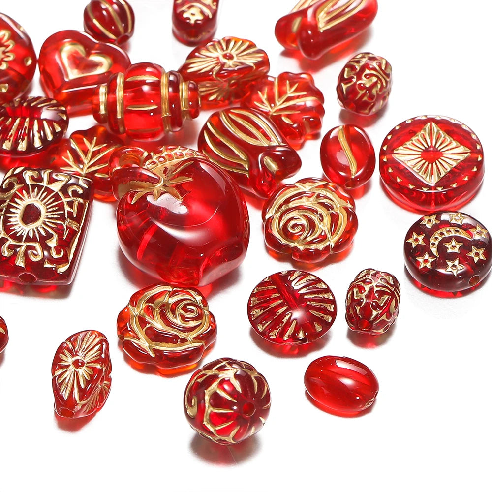 A collection of red translucent glass beads with various ornate gold foil patterns, scattered on a white background.