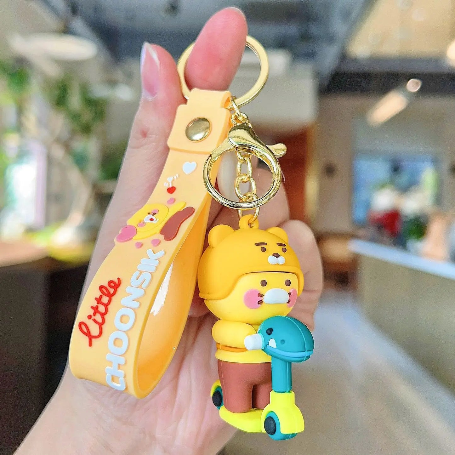 Yellow keychain with a bear character held in a hand, blurred indoor background