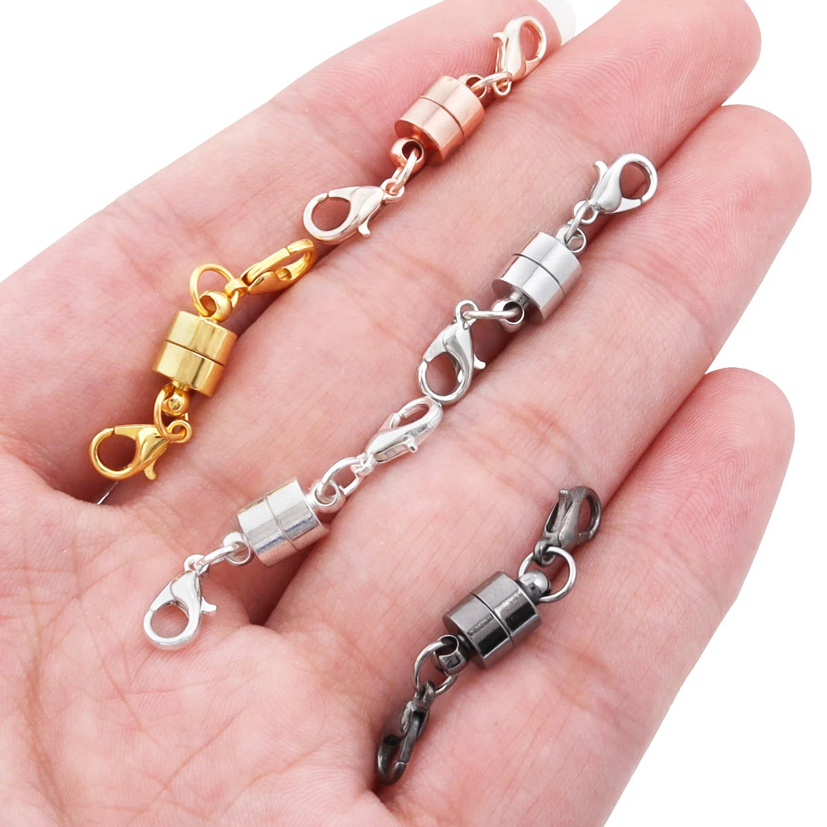 Three magnetic snap chain links with lobster clasp in gold, silver, and gunmetal gray finishes, displayed on an open hand against a white background.