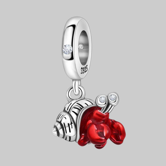 Silver charm with red snail gem and clear stones on a white background