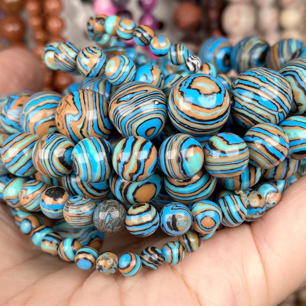 A close-up of a hand holding a stack of beaded bracelets made of round and oval beads with swirling turquoise, blue, tan, and black marbled patterns.