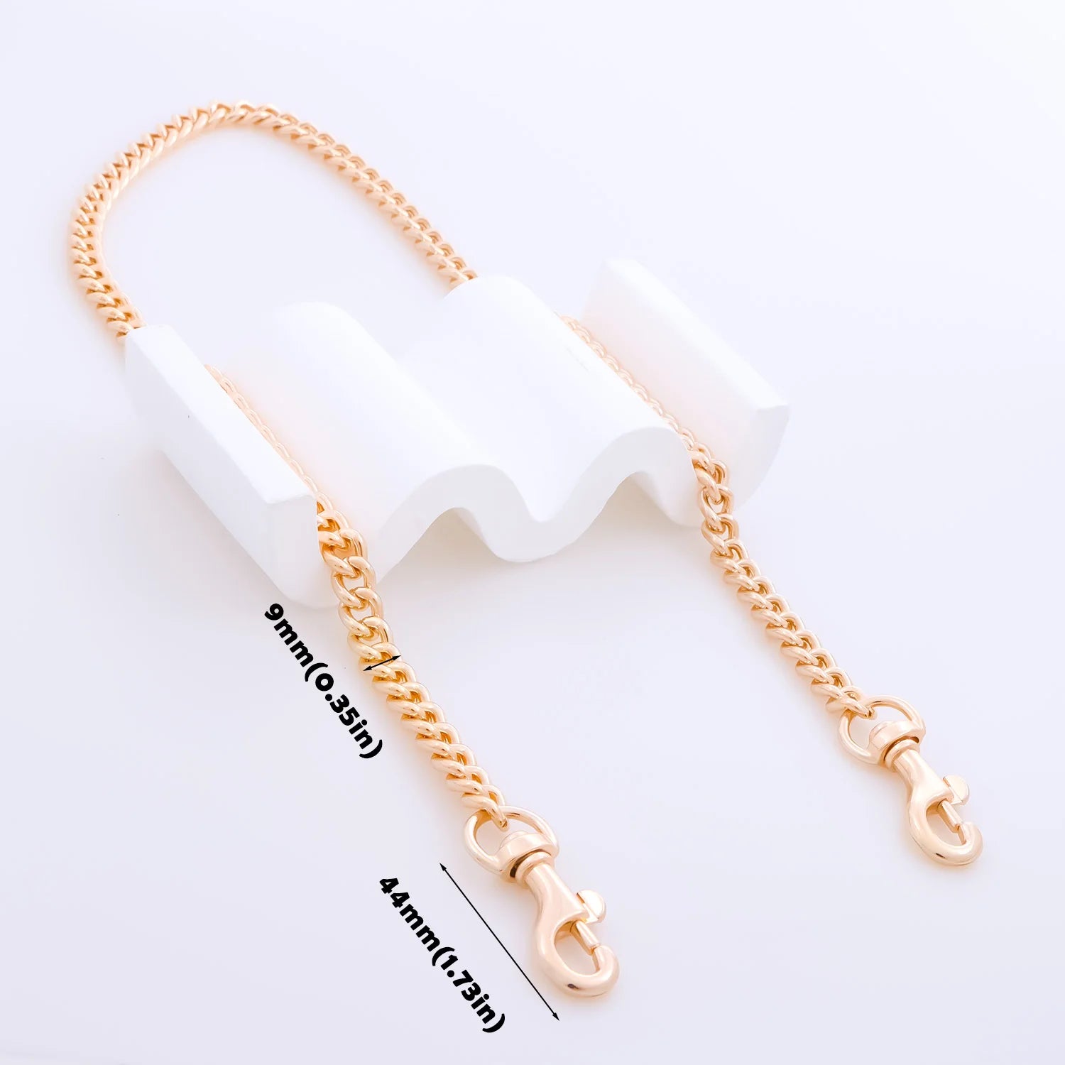 A rose gold chain accessory with two lobster clasp ends, displayed on a white wavy stand with black measurement text indicating 9mm (0.35in) and 44mm (1.