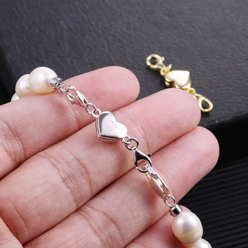 Pearl bracelet with silver heart charm held in a hand against a dark background