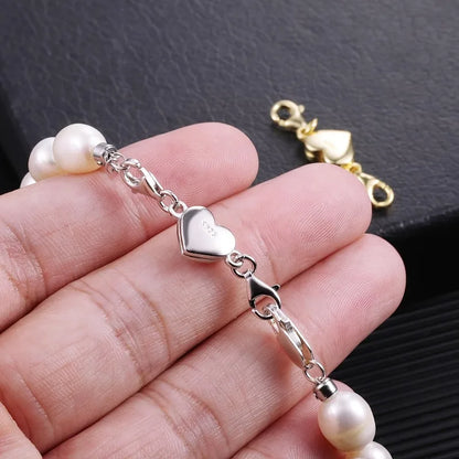 Pearl bracelet with silver heart charm held in a hand against a dark background