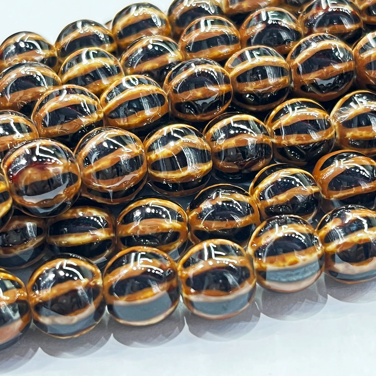 A close-up of glossy, round beads with a striped pattern of black, dark brown, and warm golden-brown.