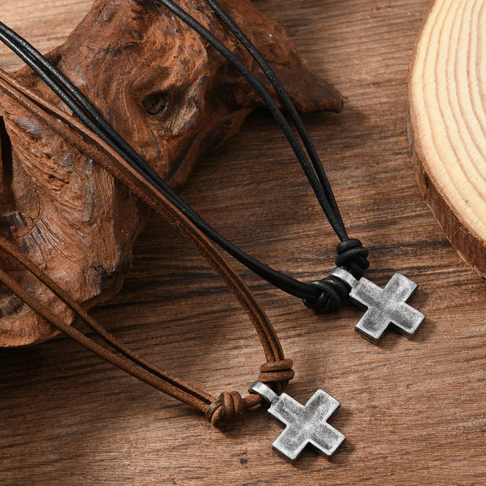 Two cross-shaped pendants on leather and cord straps on a wooden surface.