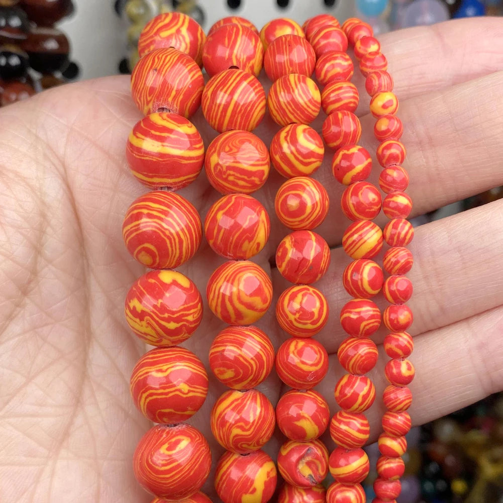 Several strands of glossy round beads in red-orange and yellow marbled swirl patterns, held in a person's hand.