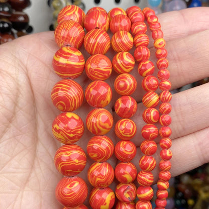 Several strands of glossy round beads in red-orange and yellow marbled swirl patterns, held in a person's hand.